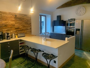 A modern kitchen with a large island, bar stools, a built-in oven, and a refrigerator.
