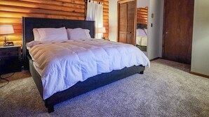 A bedroom with a wooden ceiling, a bed with white bedding, a nightstand with a lamp, and a door leading to another room. - "The Northern Star" Townhouse @ Snowshoe on Raven Golf Course (Snowshoe)