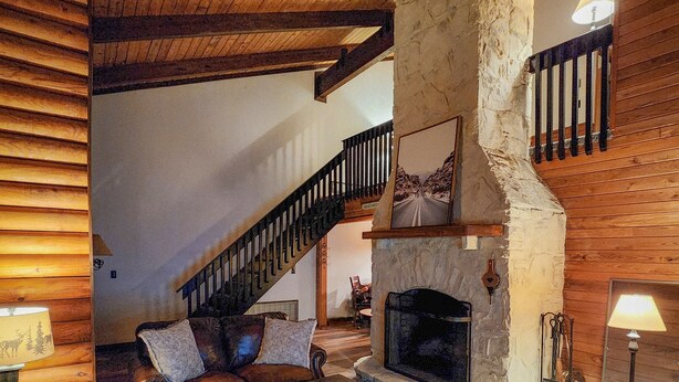A cozy log cabin interior with a stone fireplace, wooden floors, and a staircase leading to an upper level. - "The Northern Star" Townhouse @ Snowshoe on Raven Golf Course (Snowshoe)