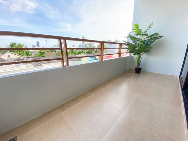 A balcony with a view of a cityscape, a potted plant, and tiled flooring.