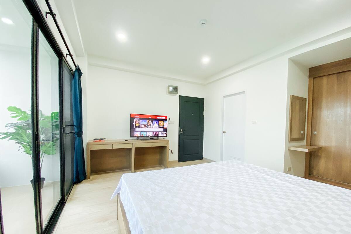 A bedroom with a bed, a desk, a television, and a door.