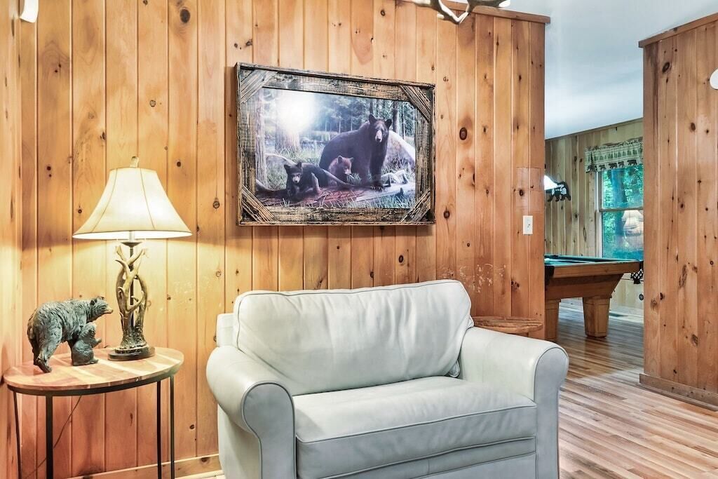 A room with wooden panel walls, a white leather sofa, a framed wildlife photograph, a lamp, and a pool table.