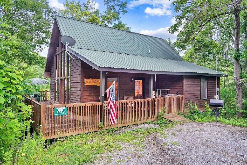 A rustic cabin with a metal roof, a wooden porch, and an American flag.