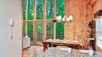 A wooden interior with a dining table set for four, large windows, and a wooden ceiling.