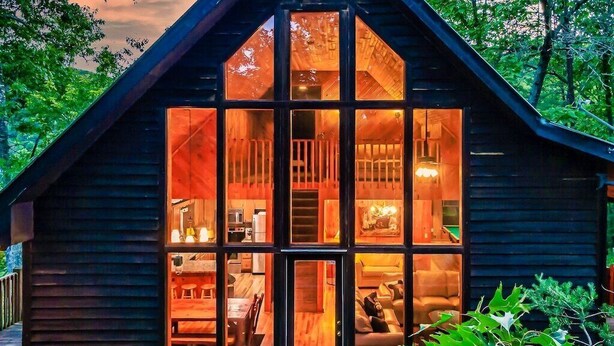A cabin with a large glass front, wooden interior, and a deck area. - 🛏️ Knotty Nice | Sleeps 11 in 2BR + Game Room + Hot Tub 🏔️ (Sevierville)