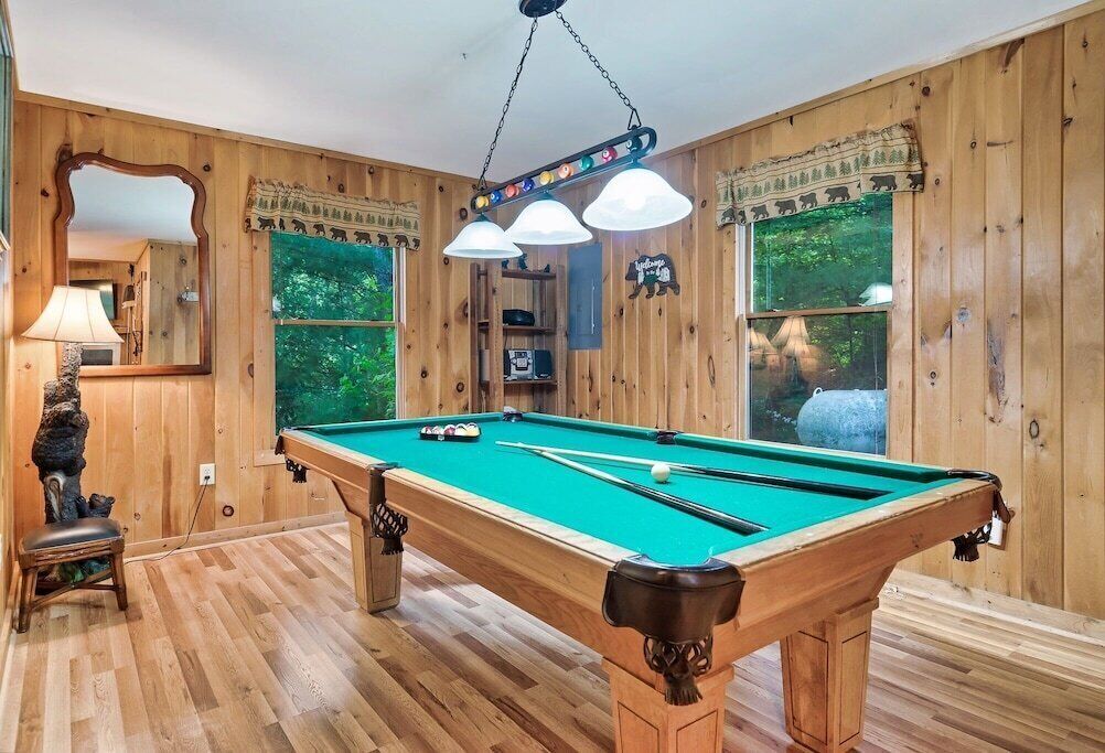 A pool table in a wooden room with a lamp, a chair, and a mirror.