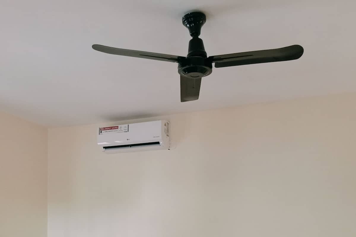 A room with a bed, a bench, a ceiling fan, and an air conditioning unit.