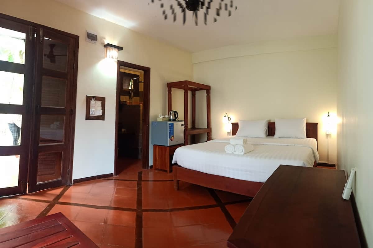 A hotel room with a bed, bedside table, nightstand, lamp, and a wooden wardrobe.