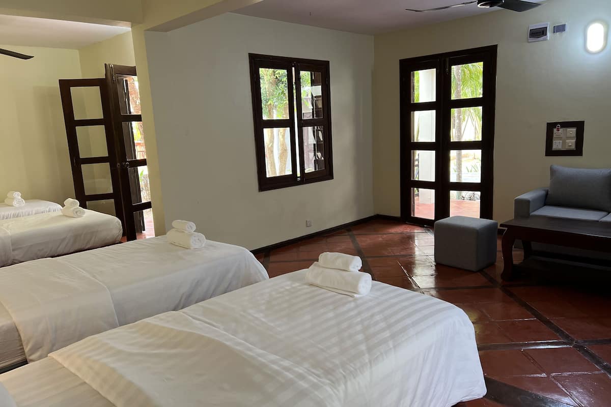 A hotel room with two beds, a sofa, a small table, and a ceiling fan.