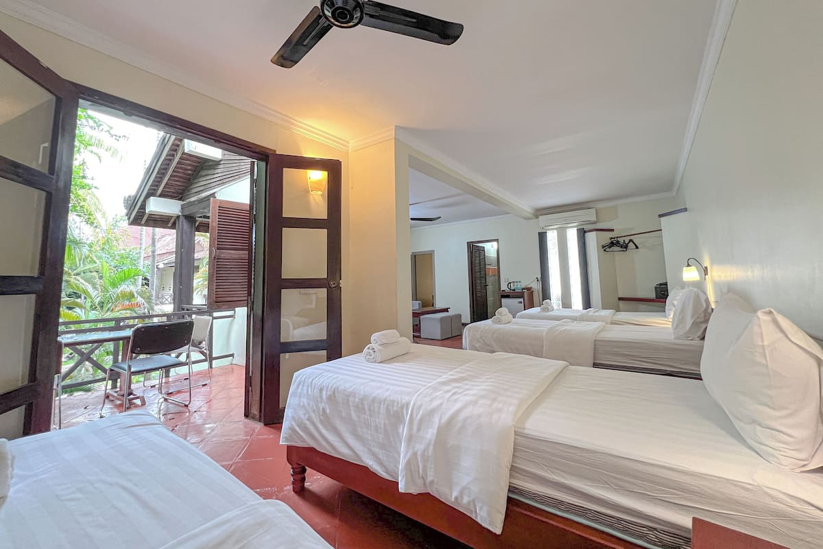 A hotel room with two beds, a ceiling fan, a desk with a chair, and a balcony with a table and chairs.