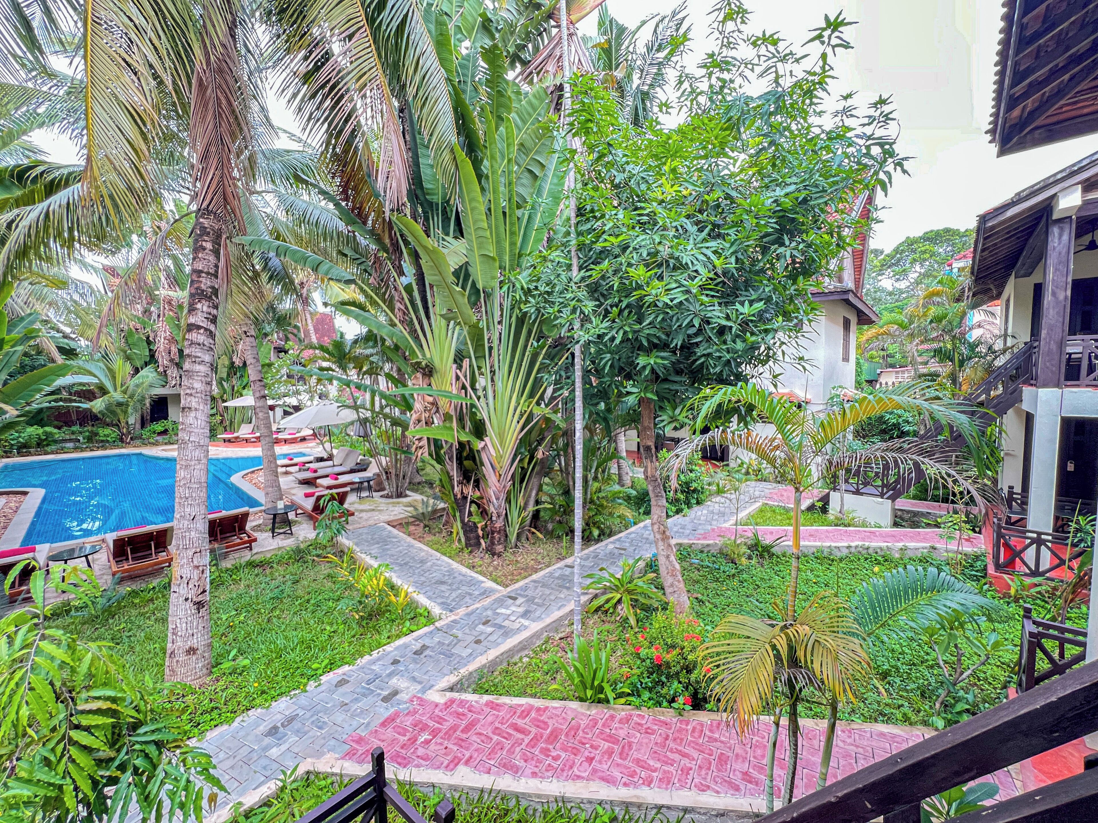 A pool area with lounge chairs and a small garden with palm trees and plants.