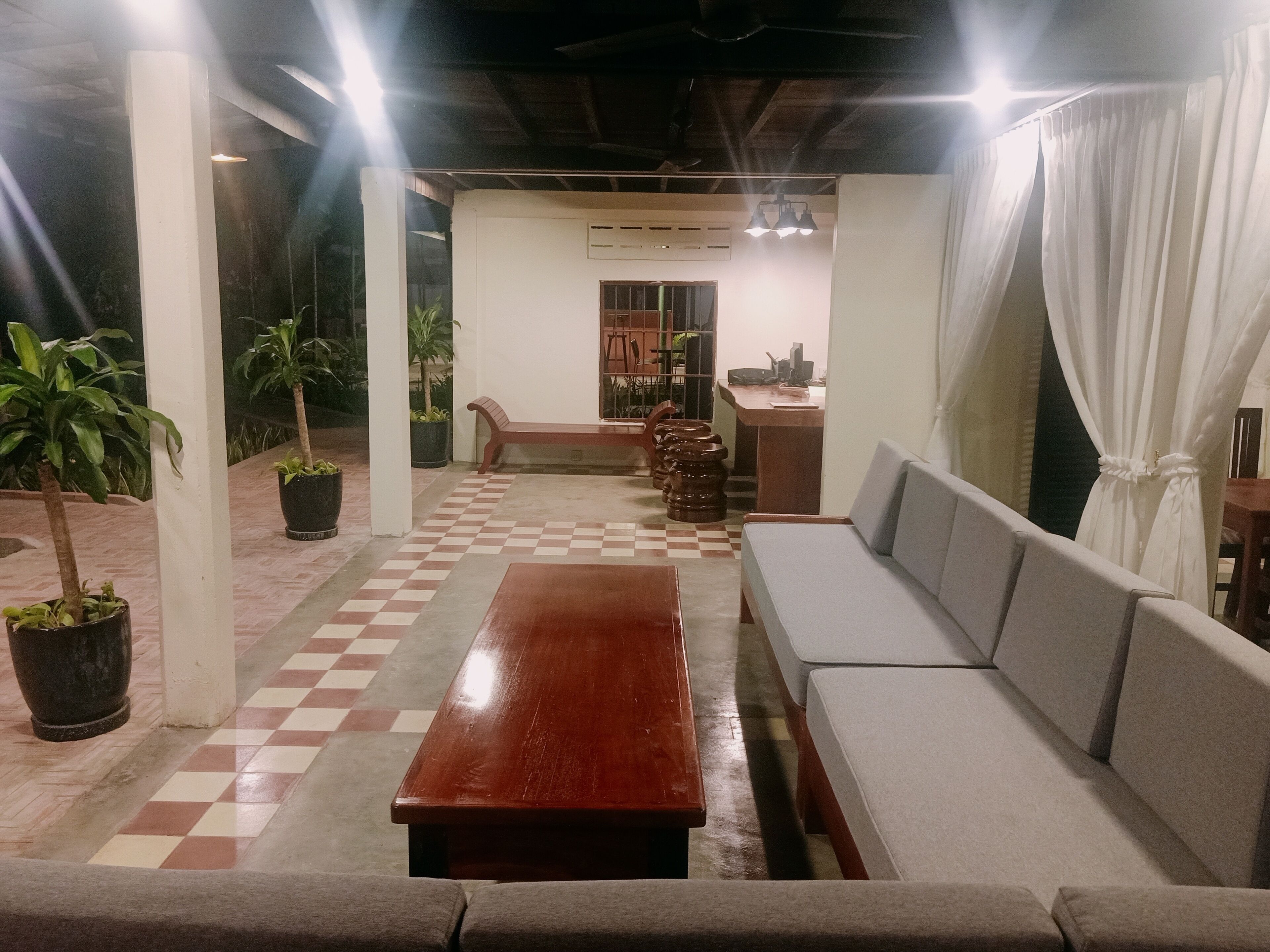 A covered outdoor seating area with a checkered floor, a wooden table, and a sofa.
