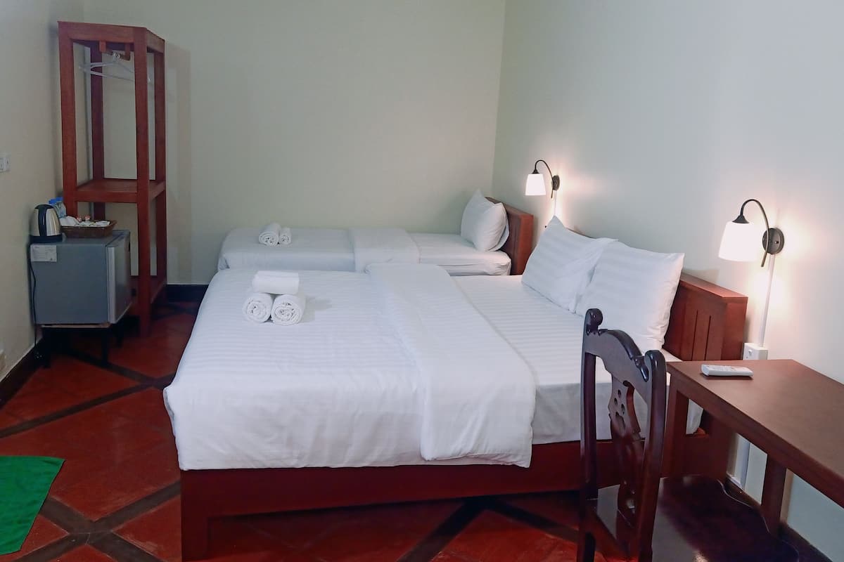 A hotel room with two beds, a wooden nightstand, a desk, a chair, a desk lamp, and a small table with a basket.