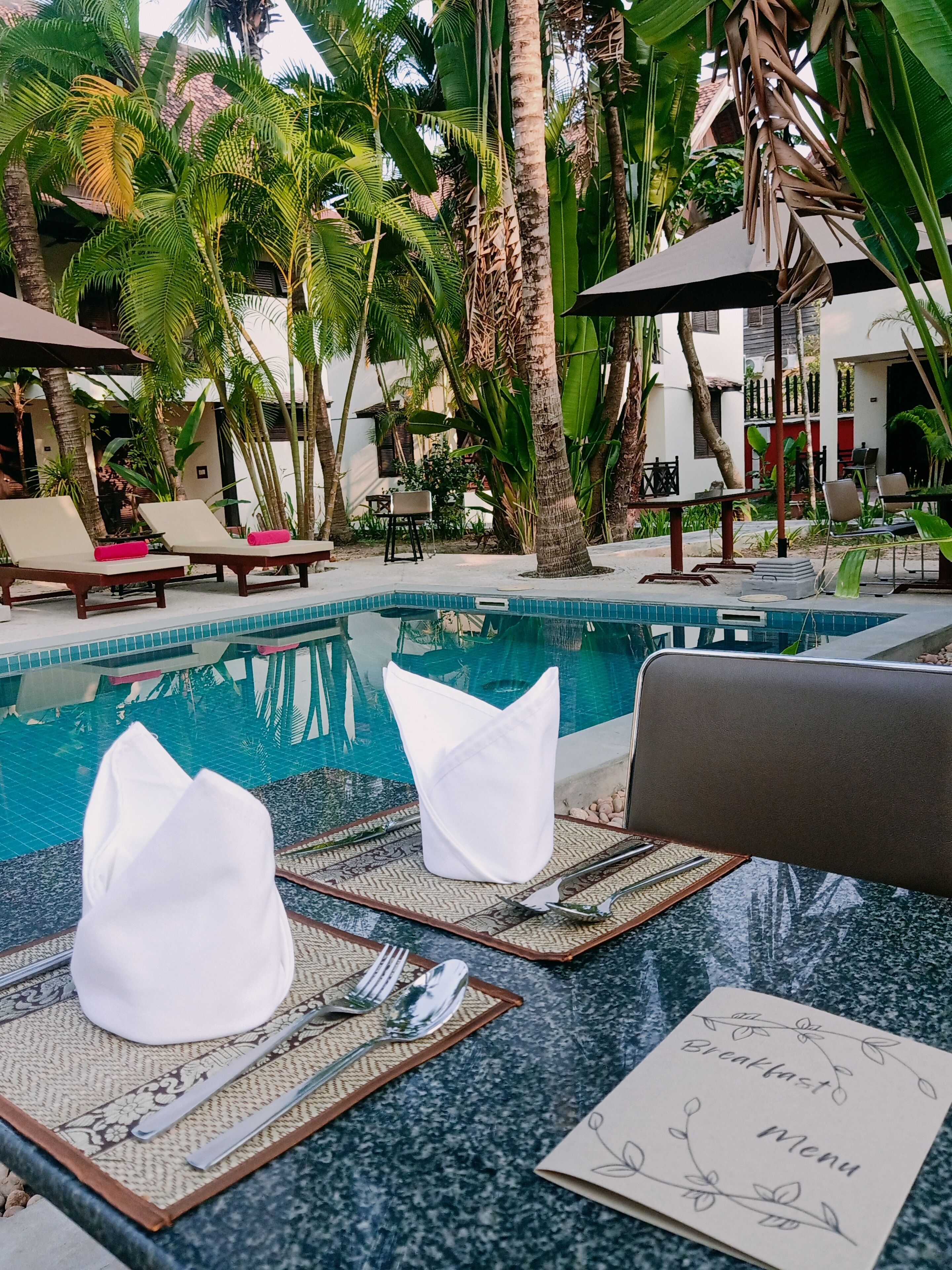 Un área junto a la piscina con sillones de descanso, una mesa de comedor con una carta y una piscina.
