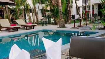 Un área junto a la piscina con sillones de descanso, una mesa de comedor con una carta y una piscina.