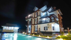A multi-story hotel with a swimming pool, balconies, and outdoor lighting. - Matoshree Club and Resort (Palampur)
