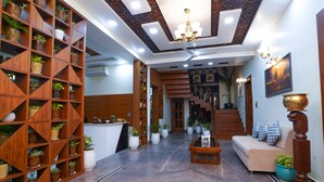 A spacious lobby with a wooden reception desk, a sofa, a coffee table, and a staircase leading to upper floors. - Matoshree Club and Resort (Palampur)