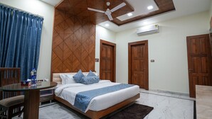 A hotel room with a bed, a round glass table, a chair, a ceiling fan, and wooden doors. - Matoshree Club and Resort (Palampur)