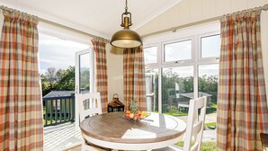 Een eetruimte met een ronde tafel, witte stoelen, geruite gordijnen en een hanglamp.