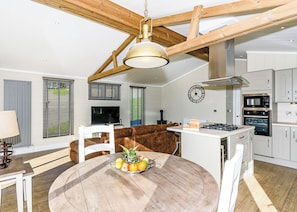 A modern kitchen with a central island, wooden ceiling beams, a round dining table with fruit, and a TV in the living area. - 1 bedroom accommodation in Bewaldeth, Keswick (Bewaldeth, Keswick)