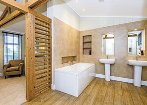 Une salle de bain moderne avec une baignoire, deux lavabos, une cloison en lattes de bois et une chaise.