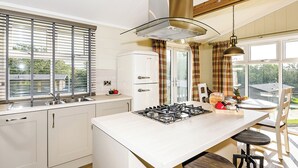 Een moderne keuken met een centraal eiland, een inbouwfornuis, een koelkast en een raam met zonwering.