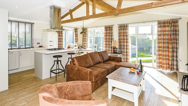 Een ruime keuken met houten balken, een centraal eiland, barkrukken, een bruine leren bank en een eettafel met uitzicht op de omgeving.