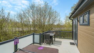 A deck with a table and chairs, a hot tub, and a view of trees and buildings.