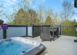 Een hottub op een houten terras met rieten meubels en een veiligheidsbord.
