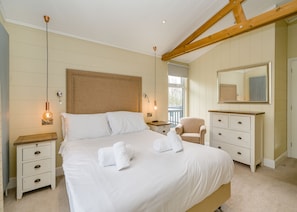 Une chambre à coucher avec un grand lit, une tête de lit en bois, des tables de chevet, une chaise, une commode et un miroir.