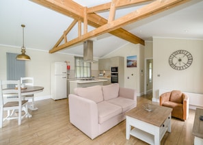 Een ruime woonkamer met een hoge plafond, een keuken met moderne apparatuur, een eettafel met stoelen en een grote wandklok.