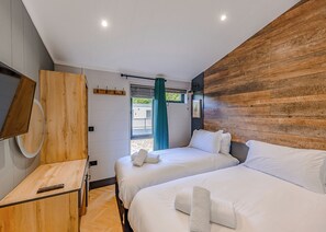 A modern hotel room with two beds, a wooden desk, a mirror, and a view of the outside.