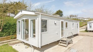 A white mobile home with large windows, a door, and a small porch. - 2 bedroom accommodation in Sandymouth Bay, Bude (Sandymouth Bay, Bude)