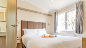 A bedroom with a bed, a tray of food, a window with curtains, and a door. - 2 bedroom accommodation in Sandymouth Bay, Bude (Sandymouth Bay, Bude)