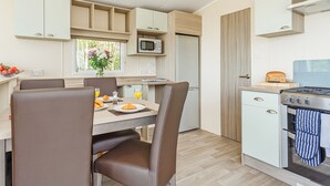 A compact kitchen with a dining table, chairs, a microwave, a stove, and a small refrigerator. - 2 bedroom accommodation in Sandymouth Bay, Bude (Sandymouth Bay, Bude)