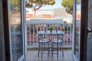 Ein Balkon mit Tisch und Stühlen, einem Blumentopf und Blick auf ein Schiff und einen Yachthafen.