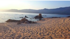 A beach with a rocky outcrop and mountains in the background.