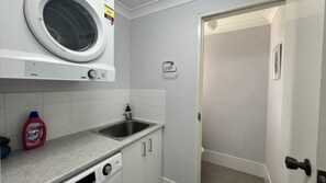 Een kleine keuken met een ingebouwde wasmachine, een spoelbak en een deur naar een andere kamer.