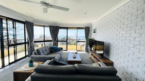 A modern living room with a grey sofa, a coffee table, and a flat-screen TV against a white brick wall.
