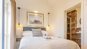 A neatly made bed with a headboard, two bedside lamps, a framed picture above the bed, and a wooden door to the right.