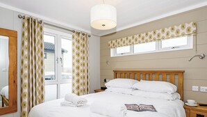 Ein Schlafzimmer mit einem hölzernen Bett, weißer Bettwäsche, einem Nachttisch mit Fernbedienung und einem Fenster mit einem gemusterten Vorhang.