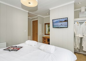 Quarto de hotel com cama, televisão, espelho e armário.
