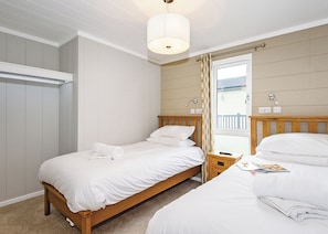 Un dormitorio con dos camas, una mesita de noche, una lámpara, una ventana con cortinas y vistas a un balcón.