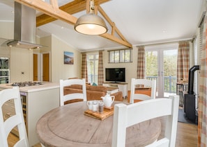 A modern kitchen with a central island, a dining area with wooden furniture, and a TV on a table.