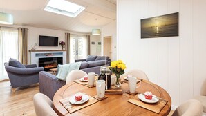 Un salon moderne avec une cheminée, des canapés, une table à manger agrémentée d’un vase de fleurs et un tableau accroché au mur.