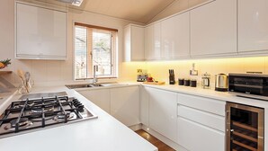 Une cuisine moderne avec des meubles blancs, une cuisinière à gaz, un four à micro-ondes et un réfrigérateur à vin.