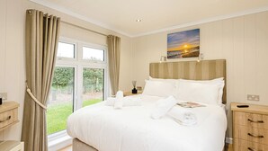 A bedroom with a large bed, a bedside table, a nightstand, a window with curtains, and a painting on the wall. - 2 bedroom accommodation in Holton Heath (Holton Heath)