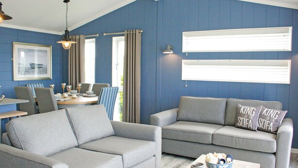 A living room with a grey sofa, a dining table with chairs, a chandelier, and a window with curtains.