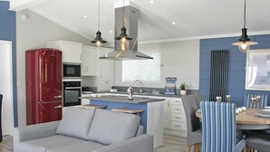 A modern kitchen with a central island, a dining area with striped chairs, a grey sofa, and a red refrigerator.