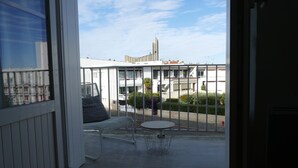 A balcony with a white chair, a small round table, and a view of buildings and a church in the background.